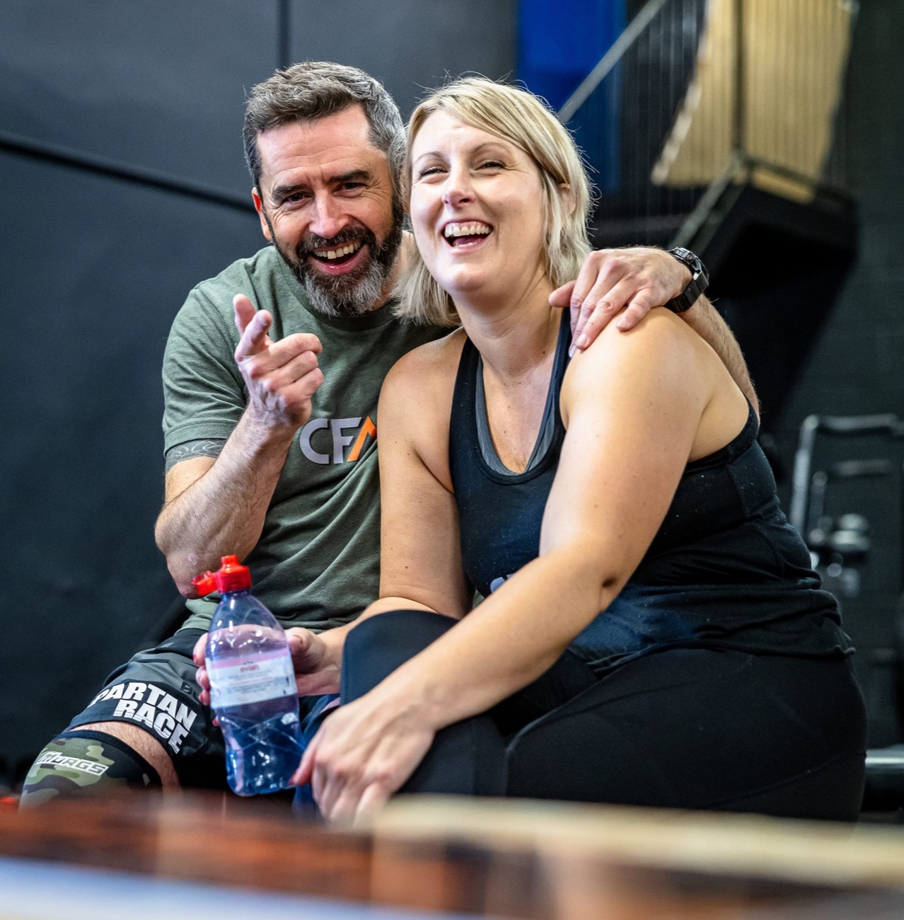 Two CrossFit Mendip members laughing together on a bench between exercises